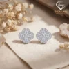 Close-up of sparkling moissanite earrings clover in platinum-plated silver resting on a neutral beige linen fabric surface