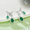 Close-up of silver pear-cut emerald drop earrings featuring shimmering cubic zirconia accents on a soft green surface