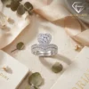 Close-up of a silver heart shaped engagement ring set with a diamond halo and matching pavé wedding band on linen fabric