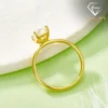 Side view of a gold plated radiant cut engagement ring resting on a white textured pedestal with a soft green backdrop