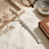 Close-up of a silver triple halo bracelet resting on a beige linen cloth next to a brown leather book and dried florals