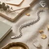 Close-up of a silver triple halo moissanite bracelet resting on beige linen fabric with dried petals and a quartz crystal