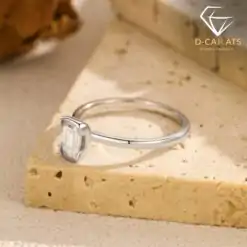 Silver band featuring a horizontal east west emerald cut moissanite stone resting on a textured beige travertine stone