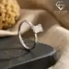 Side view of a polished silver band featuring a horizontal east west emerald cut moissanite stone on a dark stone slab