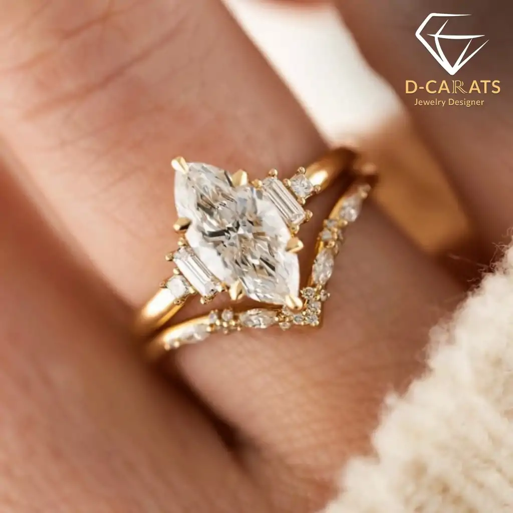 Marquise Moissanite Bridal Ring Set 15 Close-up of a gold marquise moissanite bridal ring set with baguette side stones on a finger wearing a cream sweater