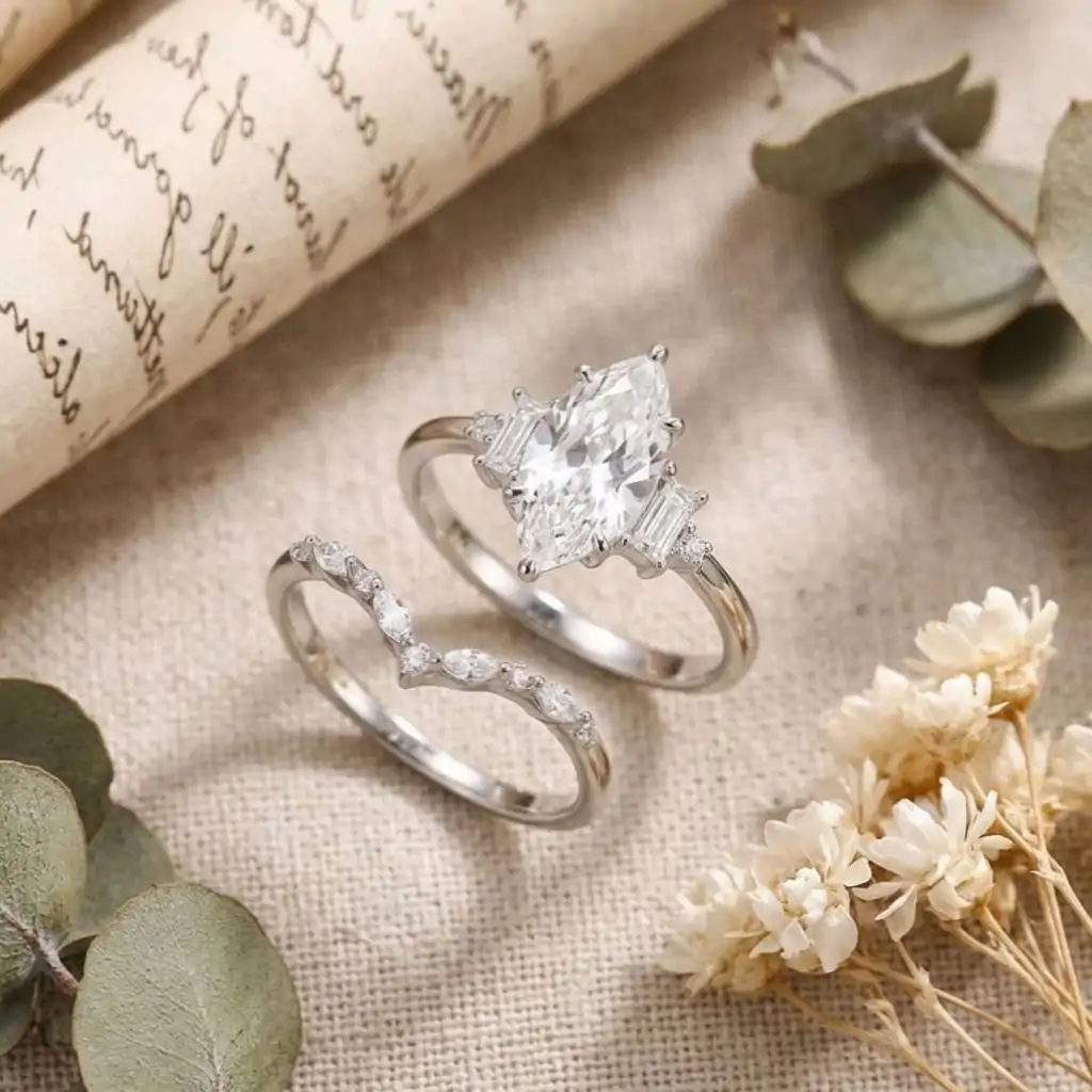 Marquise Moissanite Bridal Ring Set 16 Close-up of a silver marquise moissanite bridal ring set with a curved band resting on linen beside dried eucalyptus leaves
