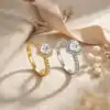Halo Heart Ring 33 Two moissanite heart ring halo designs side by side, one silver and one gold, both featuring sparkling heart-shaped stones and diamond-encrusted bands, resting on textured beige fabric with soft ribbon and dried flowers