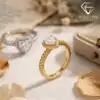 Halo Heart Ring 39 Golden moissanite heart ring halo setting with pavé band, showcased on textured fabric beside dried petals and an open jewelry box