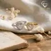 Halo Heart Ring 35 Two moissanite heart rings with halo settings, gold and silver, resting on linen beside dried flowers and an open book