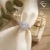Close-up of a silver heart ring double halo moissanite set against cream silk fabric with dried floral accents