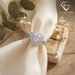 Close-up of a silver heart ring double halo moissanite set against cream silk fabric with dried floral accents