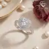 Close-up of a silver heart ring double halo set with moissanite, placed on beige linen beside a dried rose and pearls