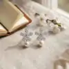 Pendientes colgantes de perla y plata con flor de circón 28 Par de pendientes colgantes de perla plateados con flores de circón sobre tela de lino neutra con flores blancas