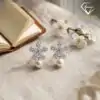 Pendientes colgantes de perla y plata con flor de circón 19 Par de pendientes colgantes de perla de plata con apliques de flores de circón sobre una tela de lino neutra con flores blancas