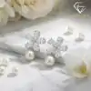 Pendientes colgantes de perla y plata con flor de circón 21 Primer plano de pendientes colgantes de perla de plata con pétalos florales de circón sobre una superficie de mármol blanco con rosas