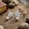 Pendientes colgantes de perla y plata con flor de circón 16 Primer plano de pendientes colgantes de perlas plateadas con pétalos florales de circón sobre una superficie de madera rústica y envejecida