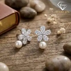 Close-up of silver pearl drop earrings featuring zircon floral petals resting on a rustic weathered wooden surface