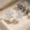 Pendientes colgantes de perla y plata con flor de circón 23 Plano detalle de pendientes colgantes de perla de plata con pétalos de circón talla marquesa y esferas crema sobre una superficie beige texturizada