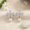 Silver pearl drop earrings with zircon flower 2 Close-up of silver pearl drop earrings featuring a sparkling zircon flower design resting on a textured cream fabric