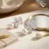 Pendientes colgantes de perla y plata con flor de circón 18 Primer plano de pendientes colgantes de perla plateada con flores de circón marquesa sobre una superficie texturizada de lino beige