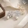 Pendientes colgantes de perla y plata con flor de circón 27 Primer plano de pendientes colgantes de perla de plata con flores de circón brillantes sobre una tela de lino crema con una cinta