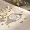 Close-up of a three stone emerald cut ring in polished 925 silver resting on beige linen beside delicate white flowers