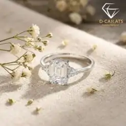 Close-up of a three stone emerald cut ring in polished 925 silver resting on beige linen beside delicate white flowers