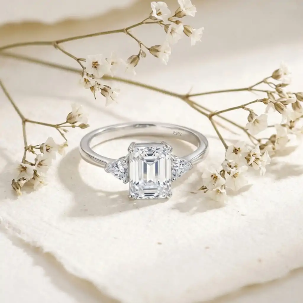 Three-stone emerald cut ring in 925 silver 8 Close-up of a three stone emerald cut silver ring nestled among delicate white dried flowers on textured cream paper