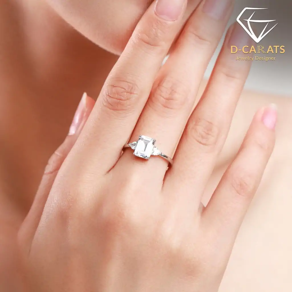 Three-stone emerald cut ring in 925 silver 7 Close-up of a polished silver three stone emerald cut ring worn on a female finger against soft skin tones